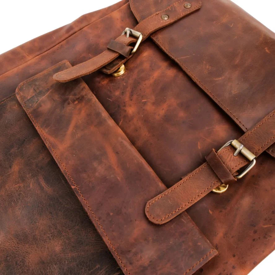 A close-up of a distressed brown leather bag with two adjustable strap closures and brass-tone buckles, shown on a plain white background.