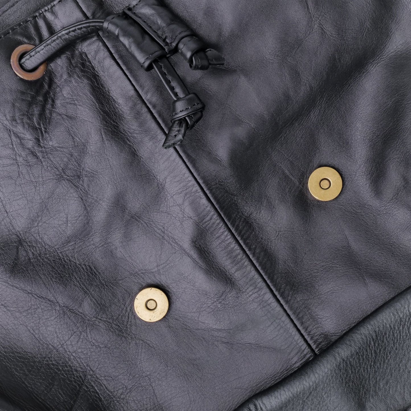 Close-up of a dark gray leather jacket with gold buttons and a drawstring.