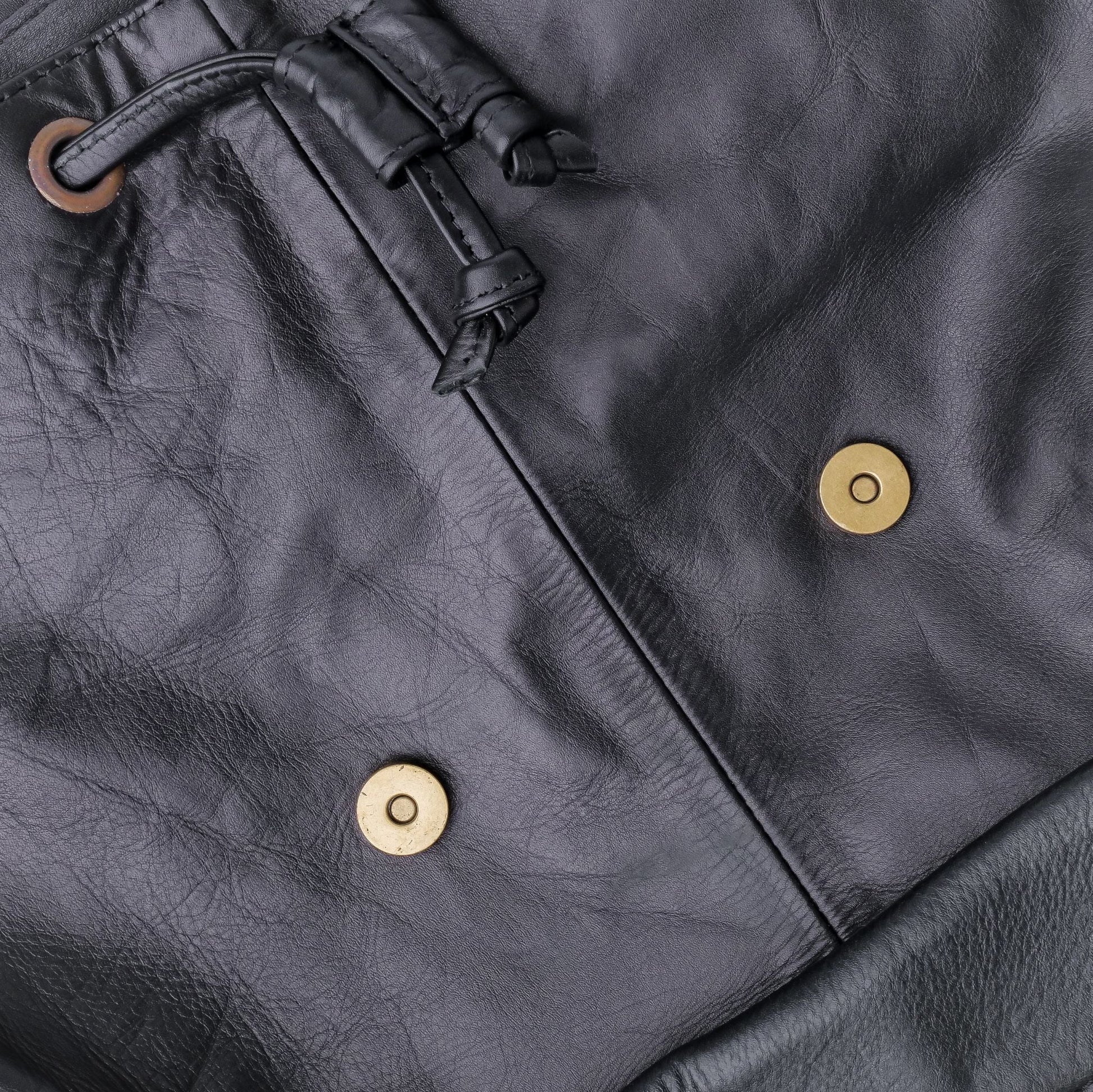 Close-up of a dark gray leather jacket with gold buttons and a drawstring.