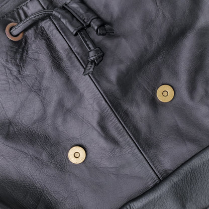 Close-up of a dark gray leather jacket with gold buttons and a drawstring.