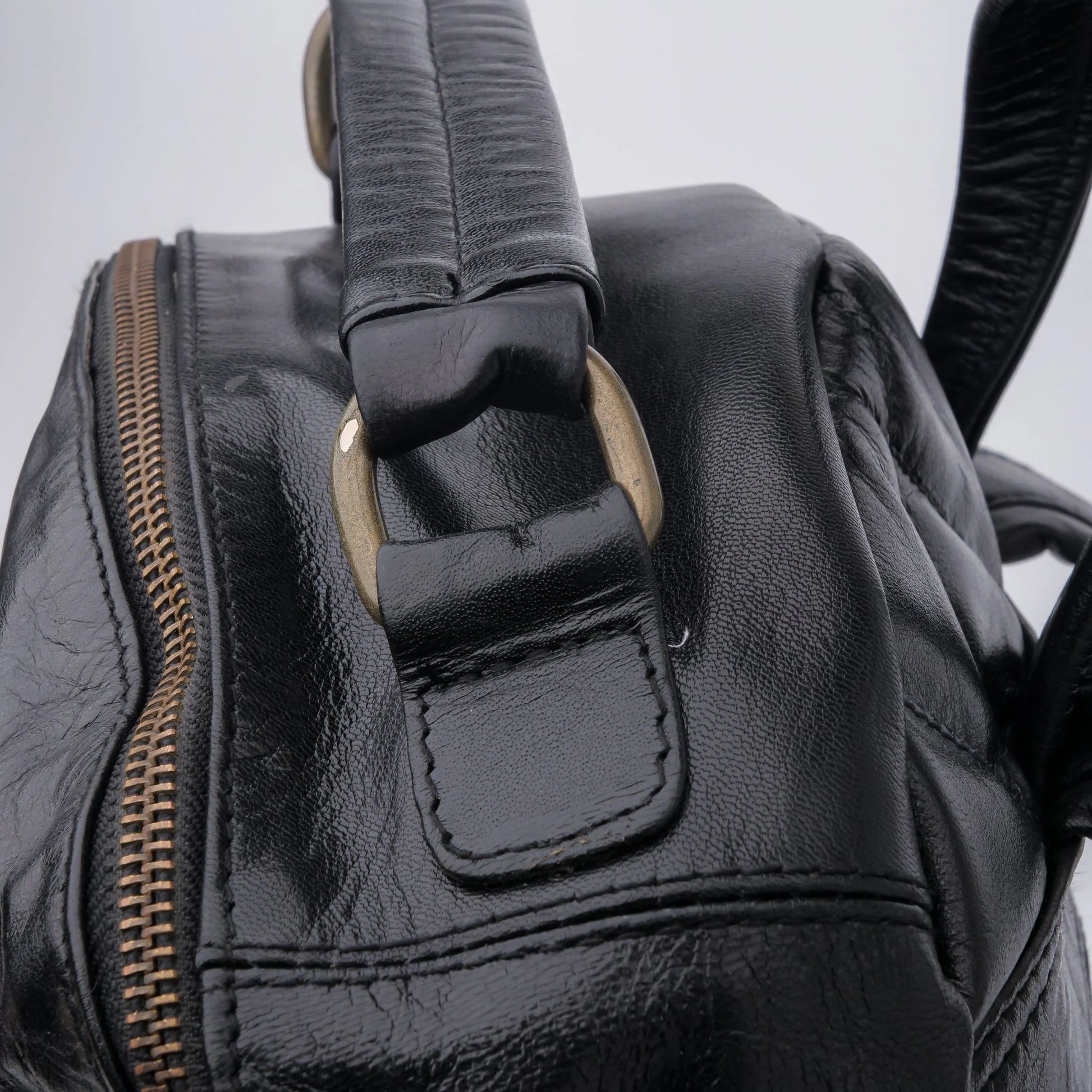 Close-up of a black leather bag with a zipper and strap on a light gray background