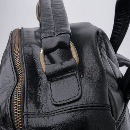 Close-up of a black leather bag with a zipper and strap on a light gray background