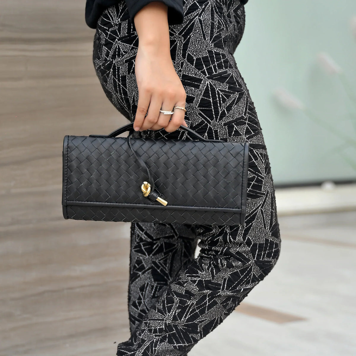 Person holding a black handbag with a patterned outfit