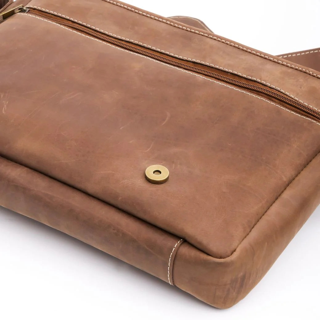 Brown leather bag with a gold zipper and button on a white background