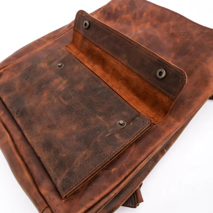 A close-up of a brown distressed leather backpack showing the interior flap, metal snap buttons, and textured leather panels on a white background.