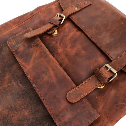 A close-up of a distressed brown leather bag with two adjustable strap closures and brass-tone buckles, shown on a plain white background.