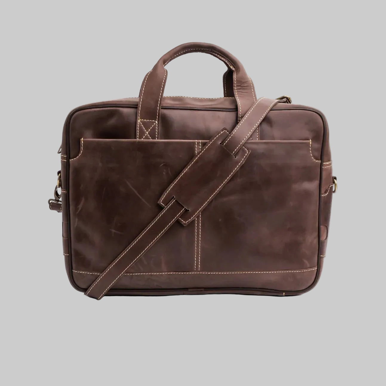 A dark brown leather briefcase with a top handle, a front slip pocket, and an adjustable shoulder strap, photographed on a white studio background.