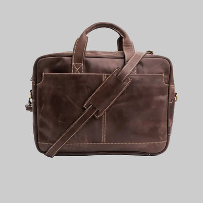A dark brown leather briefcase with a top handle, a front slip pocket, and an adjustable shoulder strap, photographed on a white studio background.