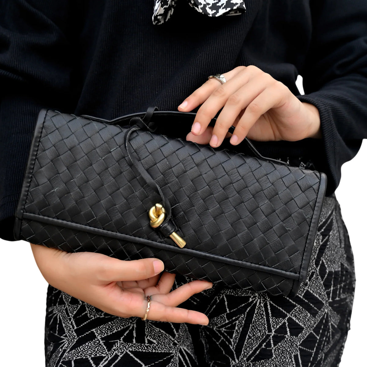 Person holding a black woven clutch bag with a gold clasp.