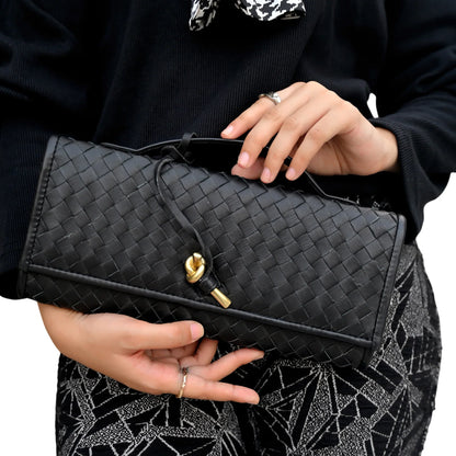 Person holding a black woven clutch bag with a gold clasp.