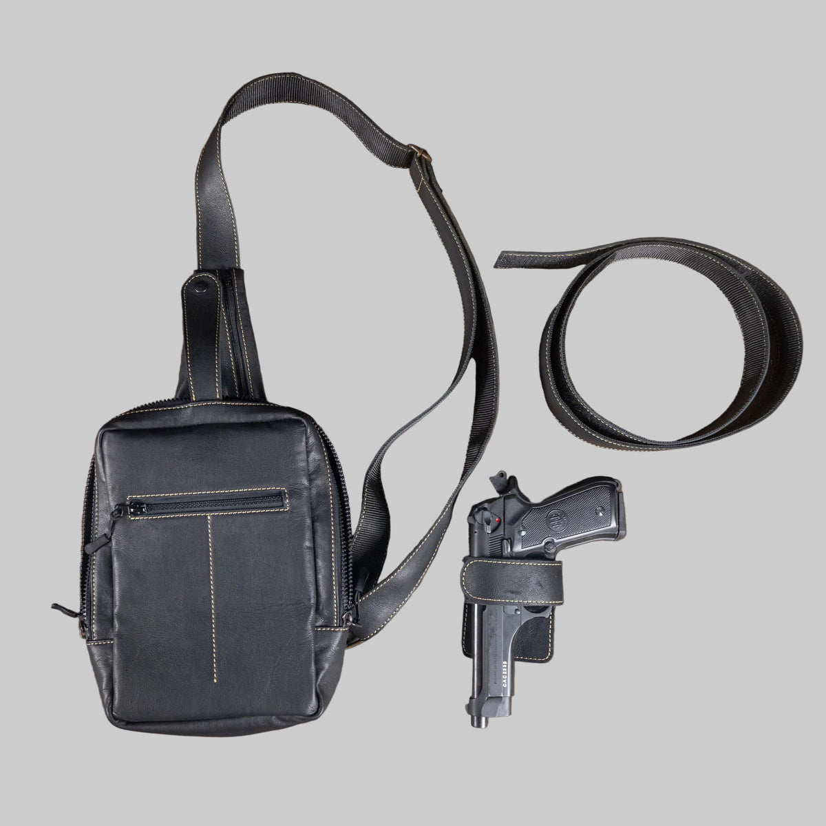 Black leather bag, gun, and belt on a wooden surface