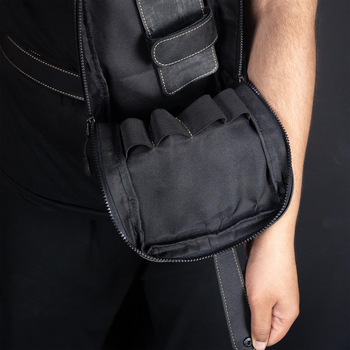 Black tactical vest with a hand holding the zipper open on a dark background