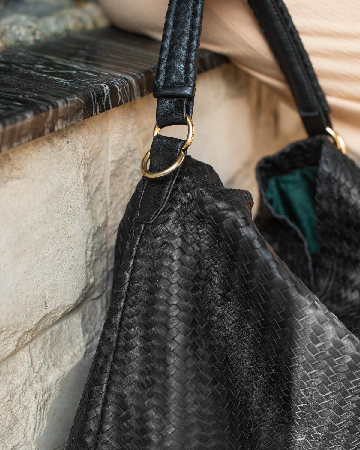 Black textured handbag with a strap on a stone surface