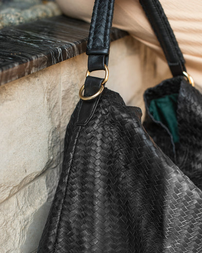 Black textured handbag with a strap on a stone surface