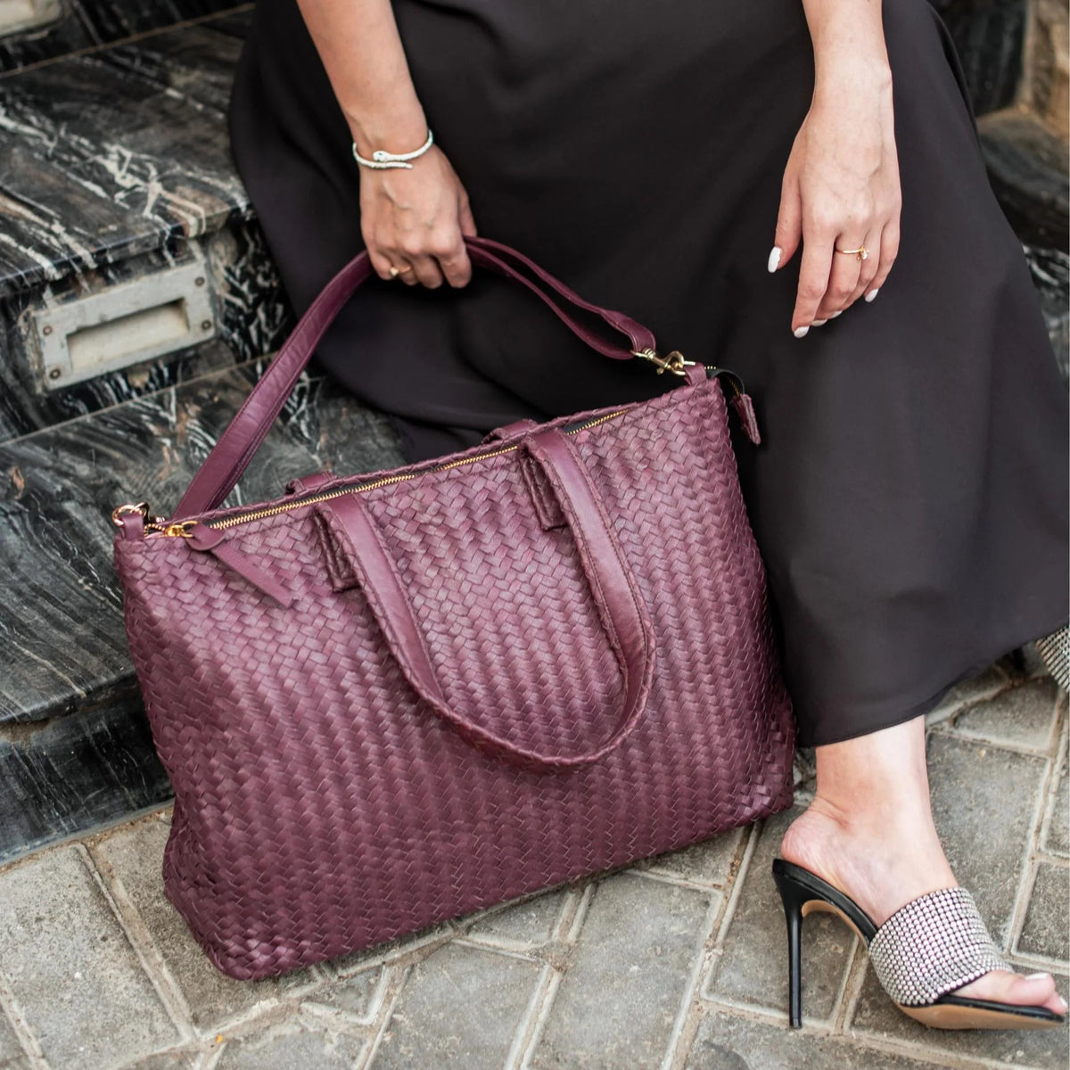 Person holding a woven purple handbag on stone steps