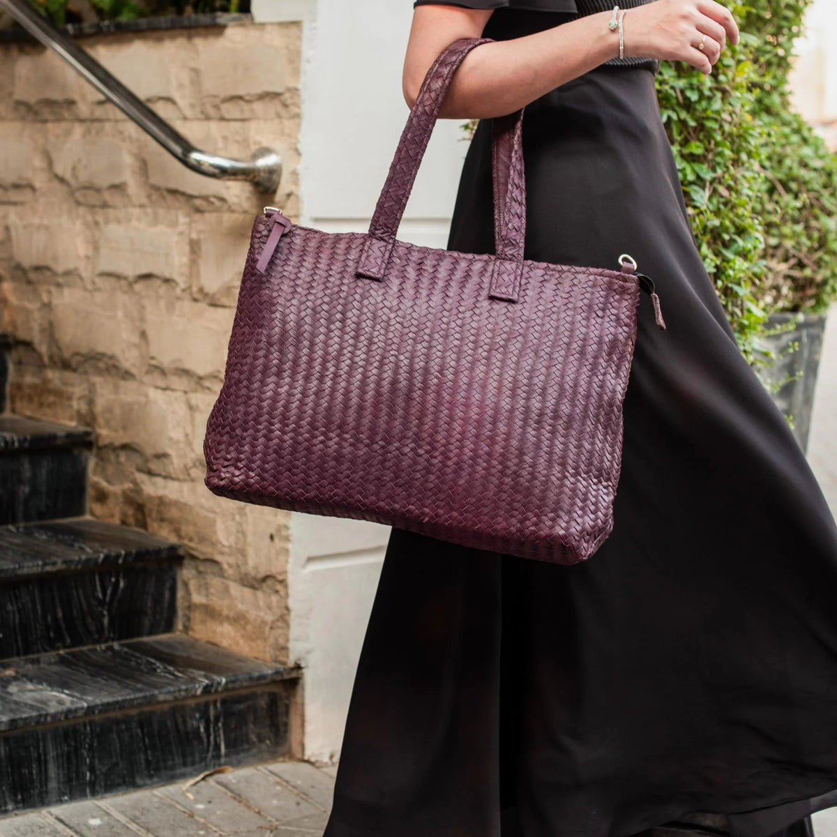 Person holding a woven purple handbag outdoors.