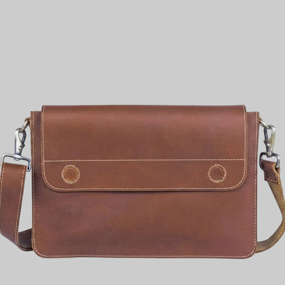 A brown leather messenger bag with a front flap pocket, two circular button details, and a matching leather shoulder strap with silver-tone metal hardware, shown against a plain white background.