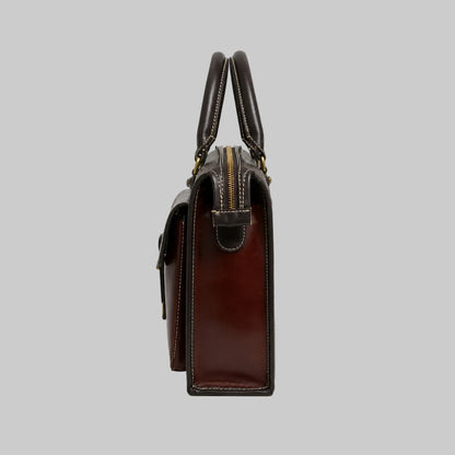 A side profile view of a dark brown leather handbag with gold-tone hardware, featuring dual top handles and a zippered top closure, set against a plain white background.