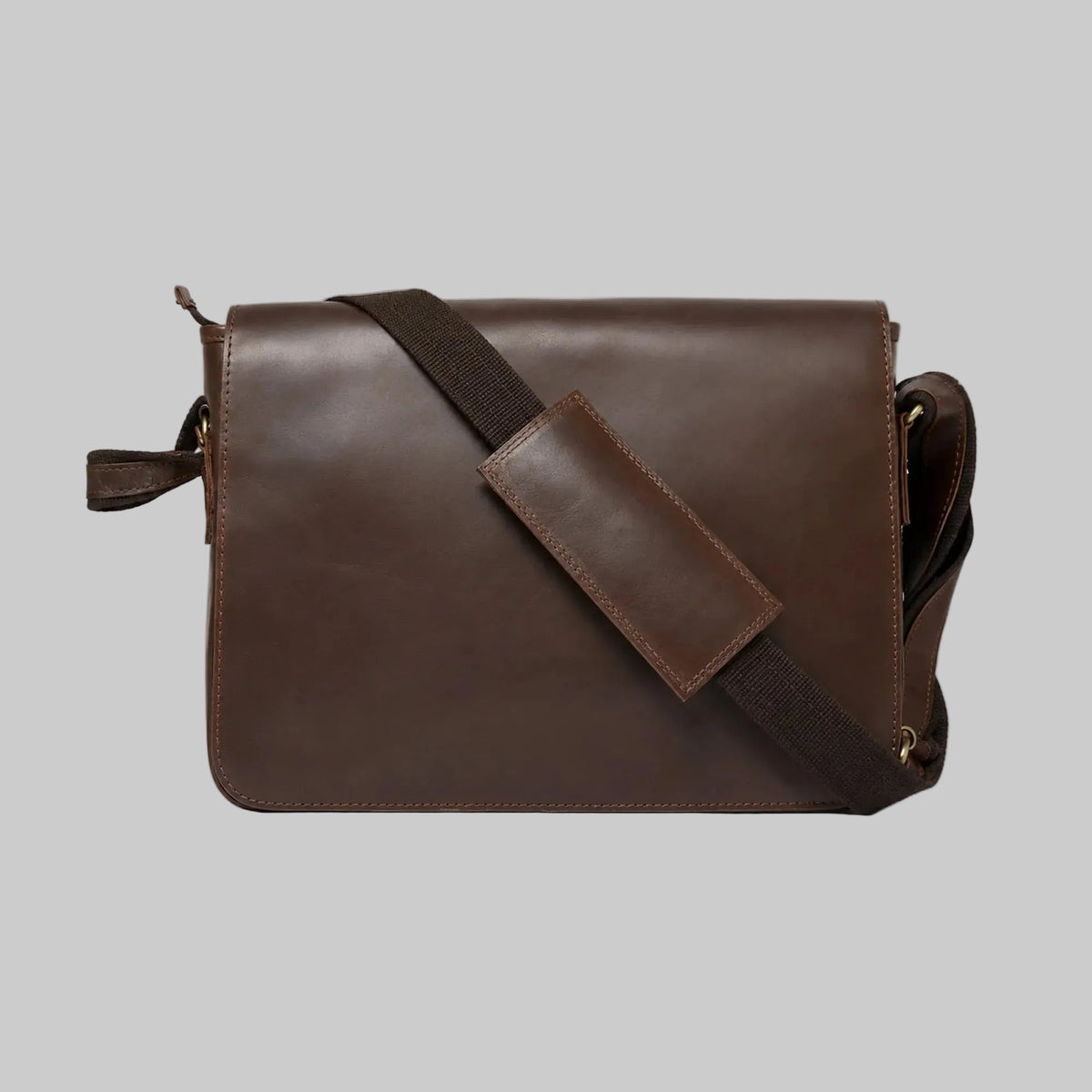 A dark brown leather messenger bag with a matching dark brown webbing strap and a rectangular leather patch, shown against a plain white background.