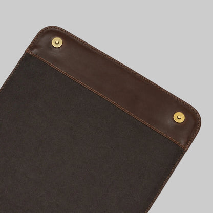 Close-up of a dark brown canvas pouch with a brown leather trim and brass snap buttons on a white background.