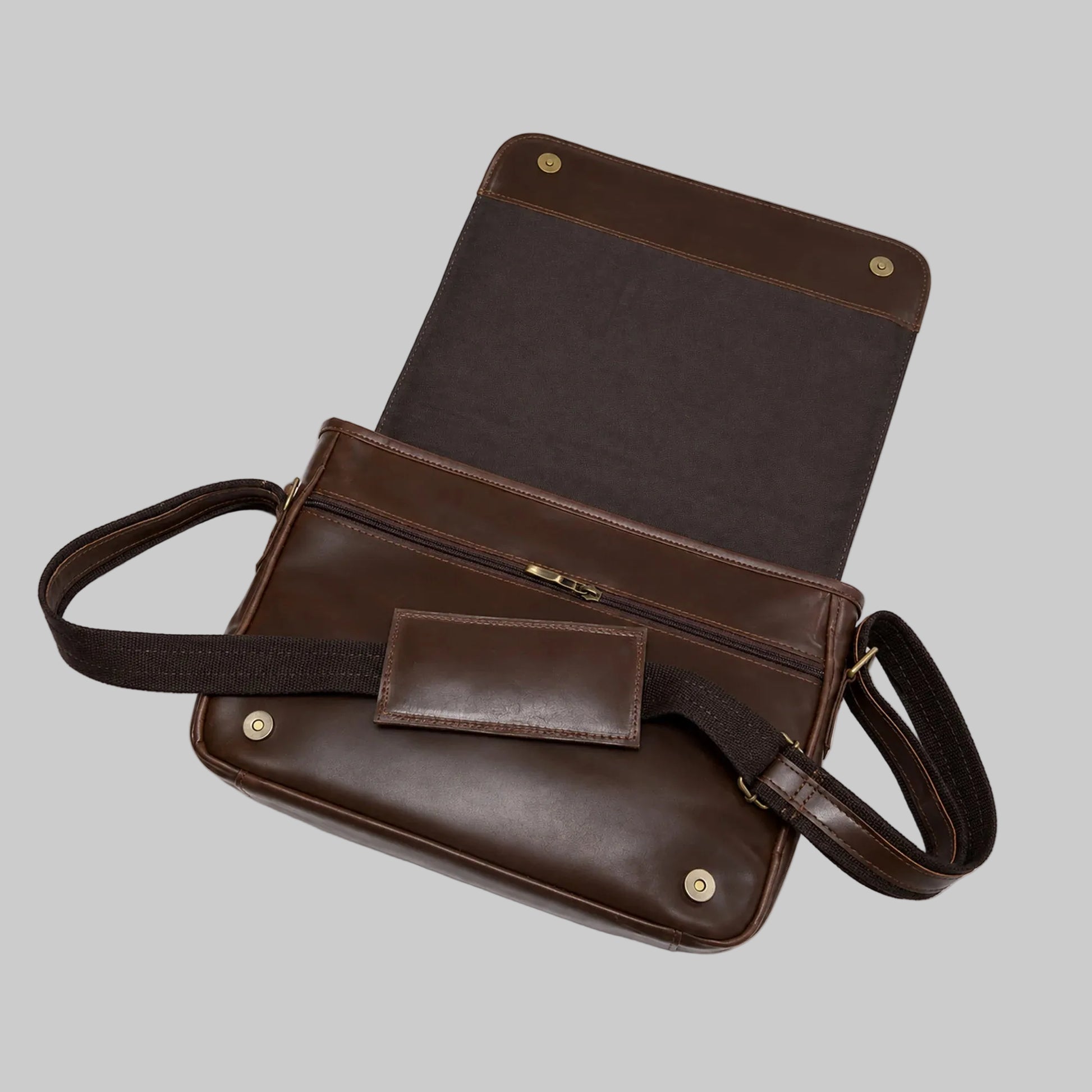 A dark brown leather messenger bag shown open, featuring a zippered front pocket, a matching leather patch pocket, and an adjustable shoulder strap, photographed on a clean white background.