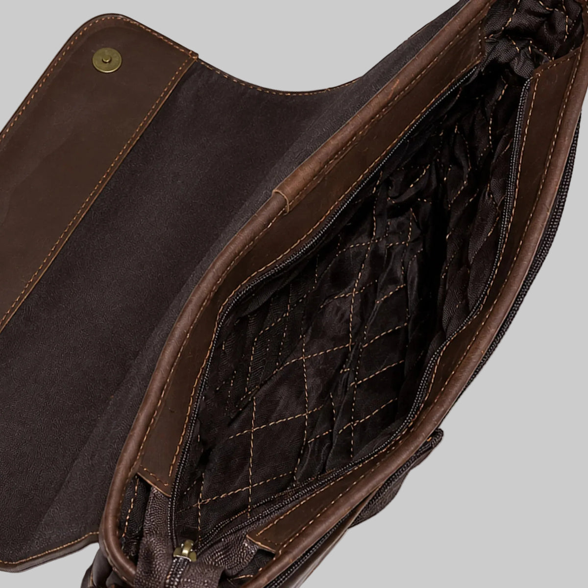 Close-up of a brown leather bag interior with a quilted dark brown lining and a gold-tone snap closure, shown on a white background.